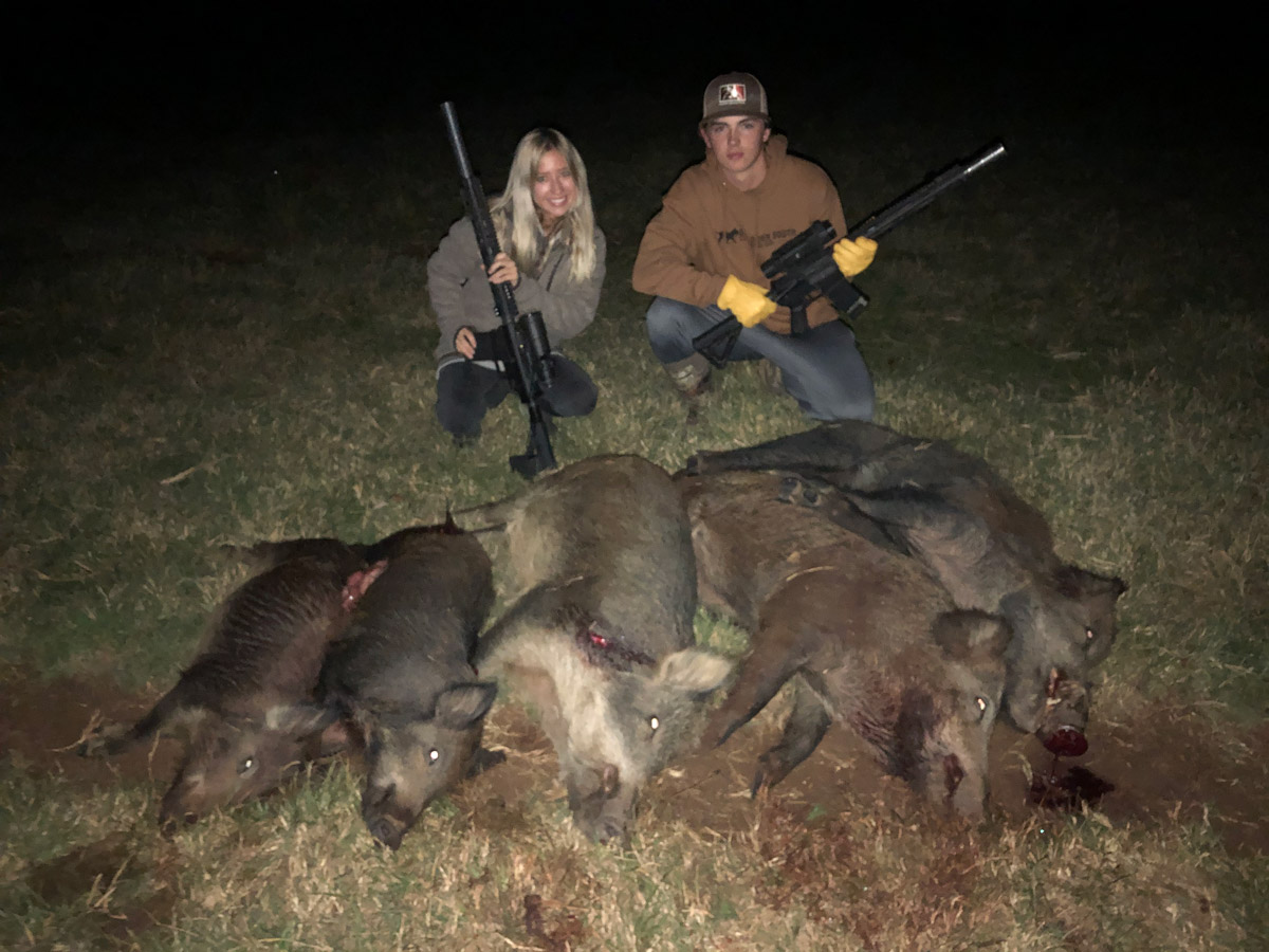 boy and girl holding rifles over dead hogs at hunt in texas