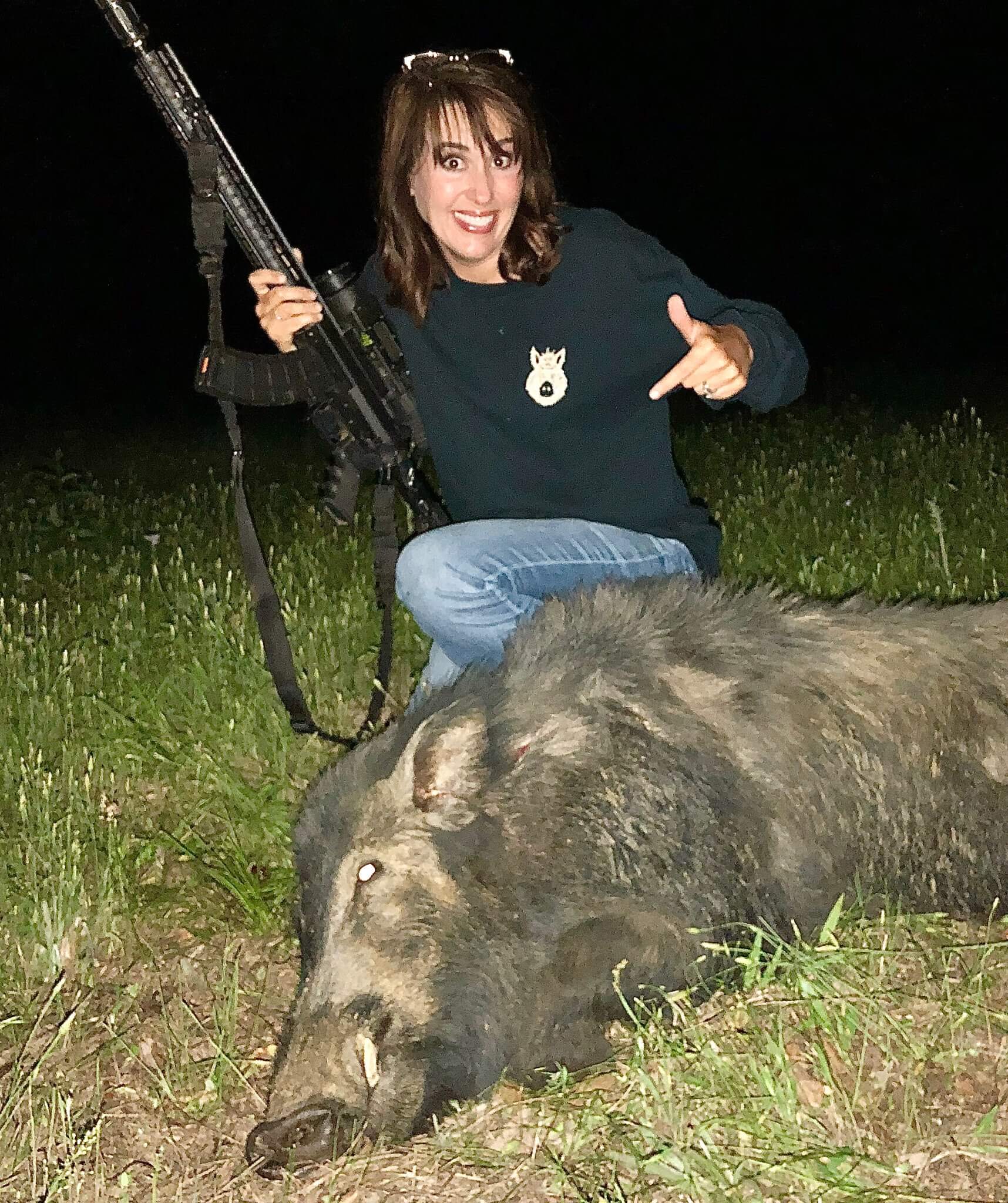 woman holding gun over killed hog at night vision hunt in texas